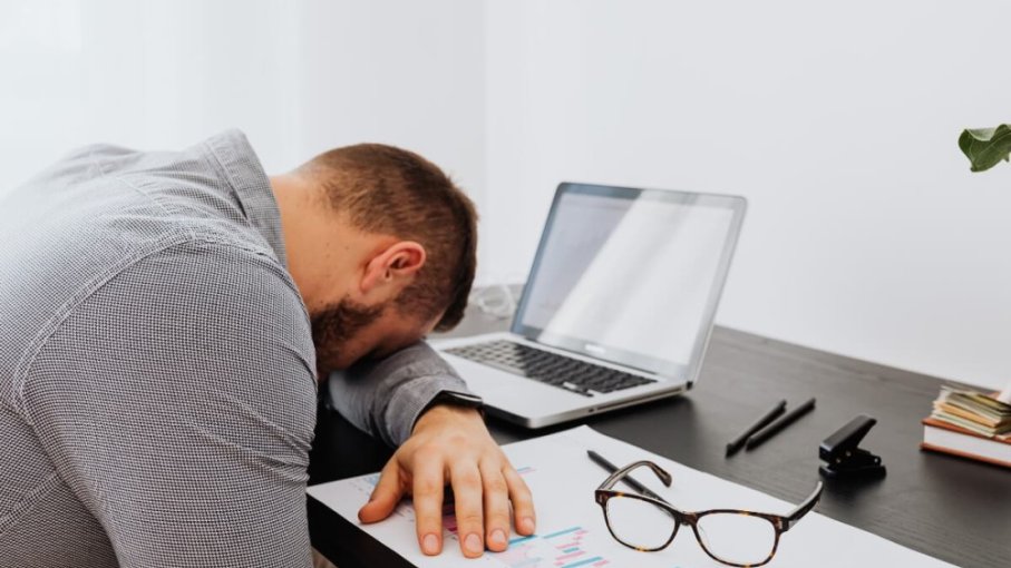 Unavený muž má položenú hlavu na pracovnom stole pri notebooku.