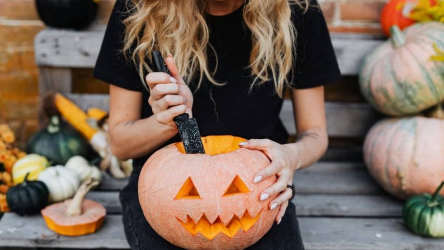 Žena vyrezáva nožom oranžovú tekvicu na Halloween.
