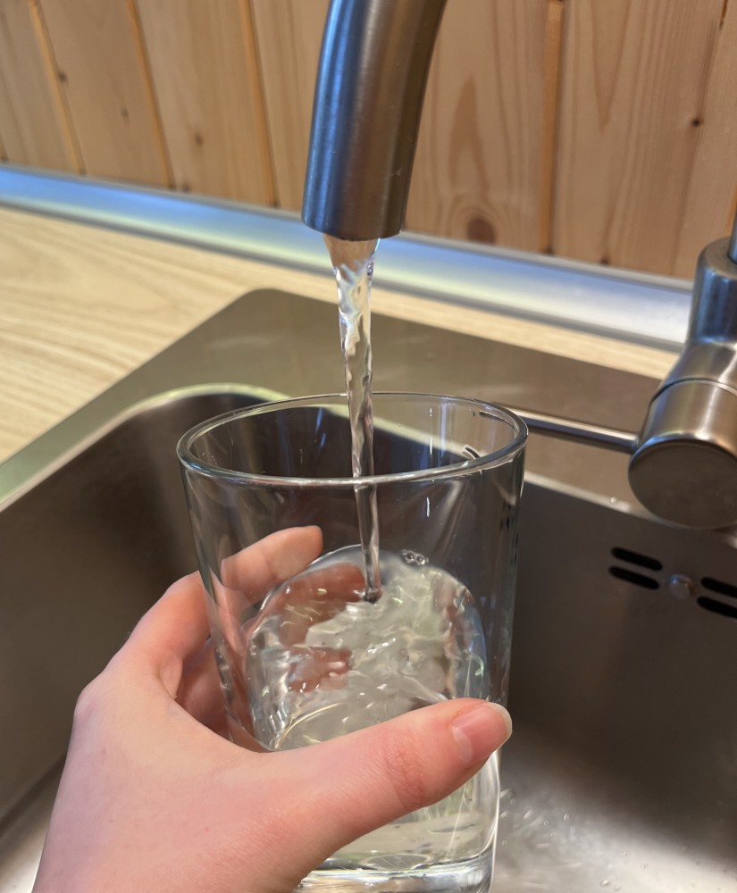Pitná studená voda tečie z kohútika do priesvitného pohára. 