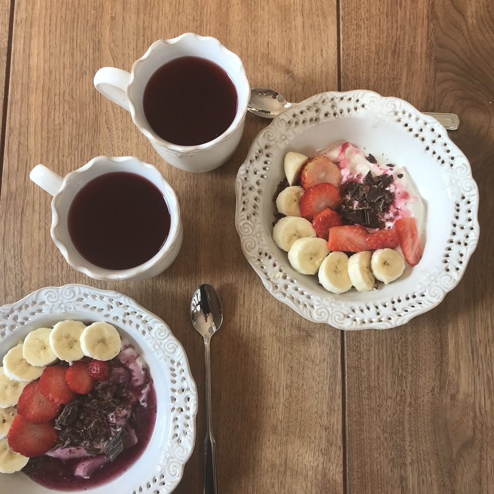 ovocný čaj a v tanieri jogurt, granola, jahody a banán na raňajky