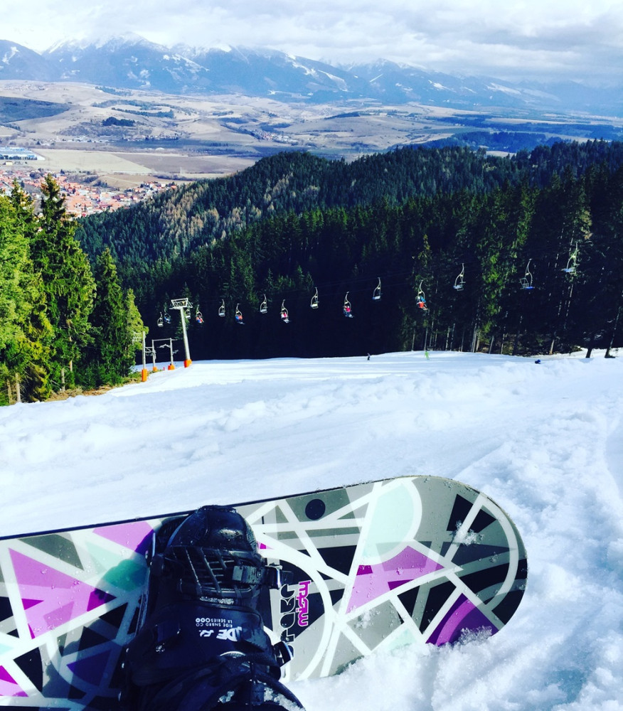 Pohľad na snowboard a zjazdovku s lanovkou a športovcami.