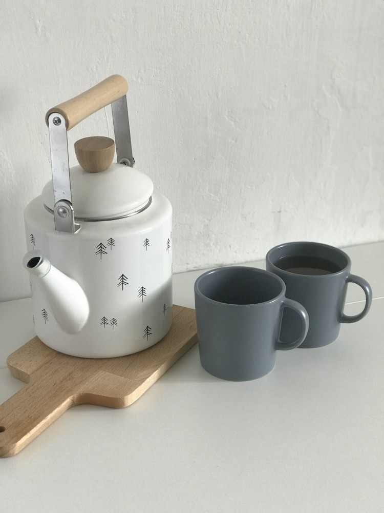 Biely čajník a dva sivé hrnčeky s čajom na bielom stole.