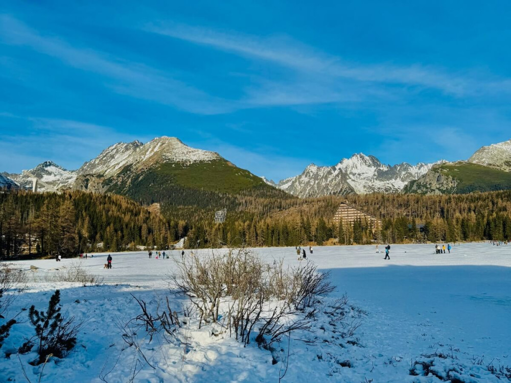 Zasnežené Štrbské pleso na ktorom sa korčuľuje veľa ľudí.