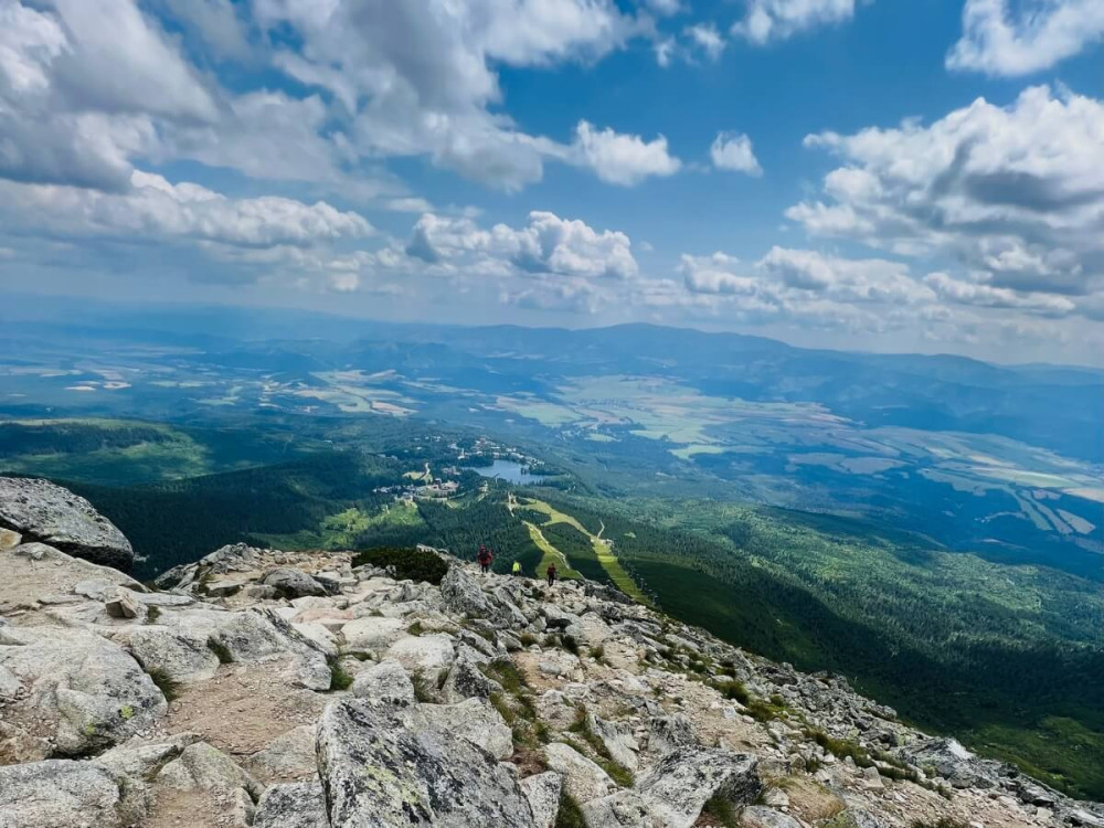Turisti kráčajú zo skalnatého kopca, okolo výhľad na zelené doliny.